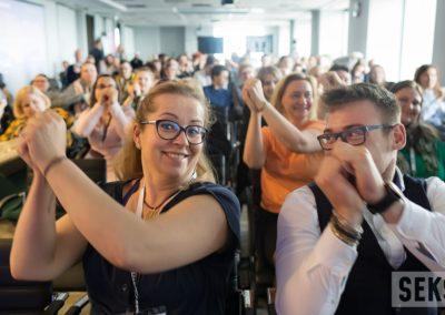 Uczestnicy konferencji podczas wspólnych ćwiczeń w trakcie przerwy, unoszą ręce do góry. Na pierwszym planie Alicja Długołęcka.