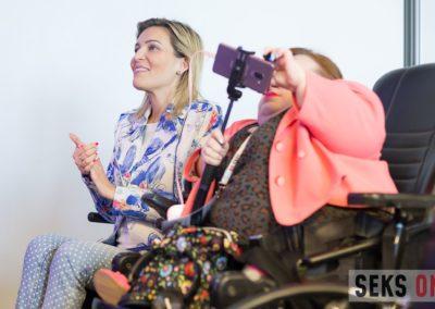 Dwie kobiety siedzą obok siebie - Agata Roczniak klaszcze, a Bogumiła Siedlecka-Goślicka robi zdjęcie telefonem.