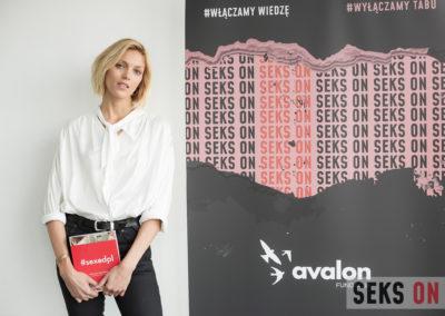 Anja Rubik stojąca obok plakatu konferencji Sekson. Trzyma książkę #sexedpl