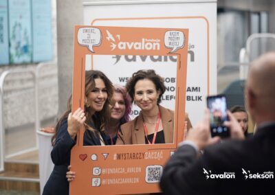 Fotograf robi zdjęcie trzem kobietom, które pozują, trzymając przed sobą ramkę z logo Fundacji Avalon.